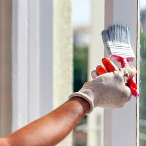 A closeup of a man painting window trim