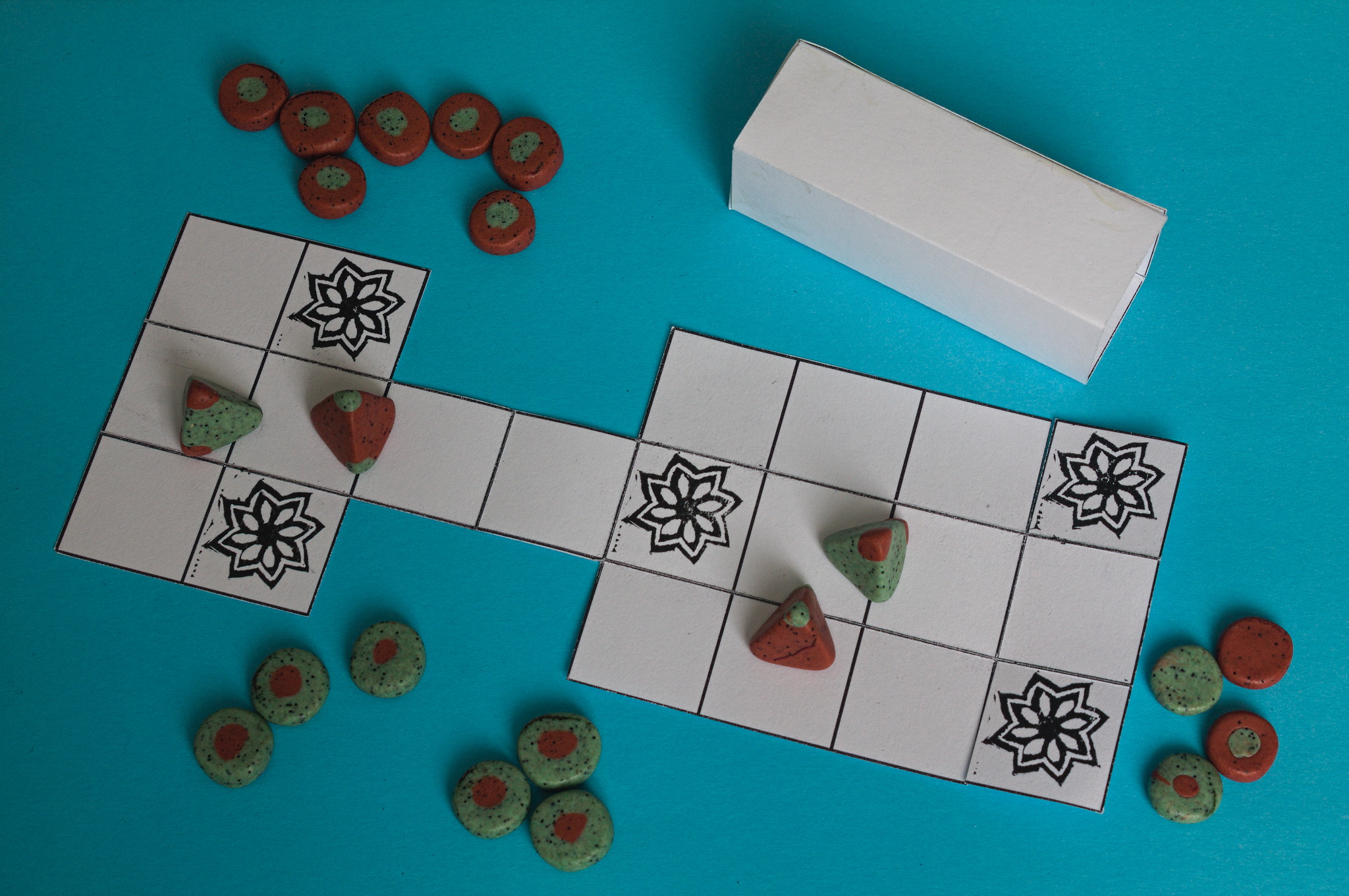 A set of red and green tokens, like the ones above, plus tetrahedron dice and four more coins with a dot of a different colour just on one side. Everything is on top of a board that folds up.