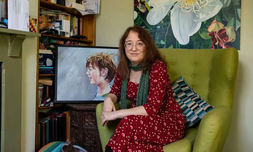 Joanne Limburg  sitting in a green chair with a painted portrait of her son next to her.