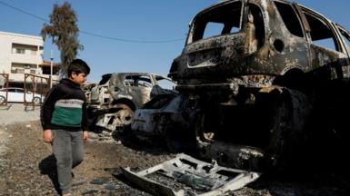 A Palestinian child walks near cars burnt near Hawara