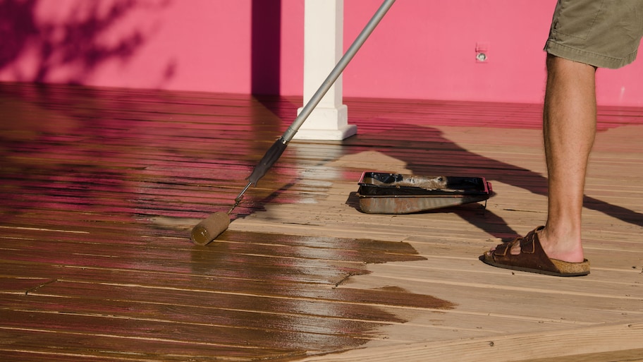 A person using a paint pole and roller to stain the deck