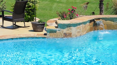 closeup of swimming pool with stone edge, concrete patio, and black lawn chair
