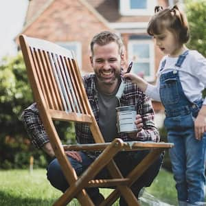 Father and daughter painting chair outside