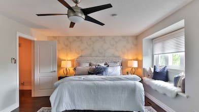 Ceiling fan in bedroom with gray paisley accent wall, gray bedding, and window seat with fur throw and pillows 