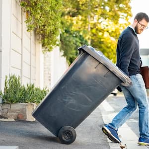 A man pulling out a wheeled dumpster