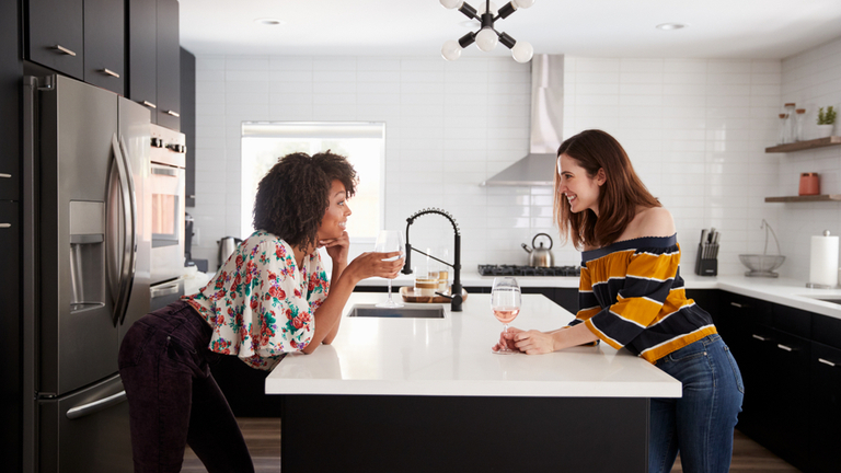 Two friends chatting in kitchen over white countertop