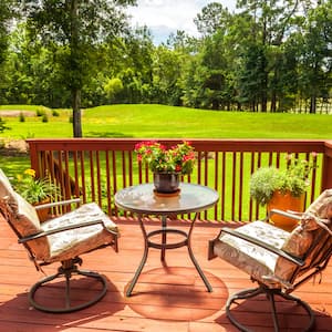 a cedar deck with two patio chairs and a small table overlooking a lush green yard