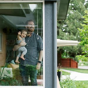 Father holding his daughter behind window of house