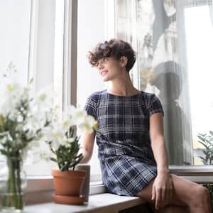 Young woman sitting on window sill looking outside