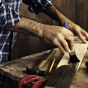  A male carpenter in a plaid shirt staining a wood plank