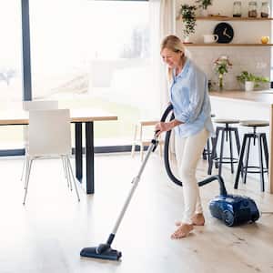 Woman vacuuming wood floor of home dining area