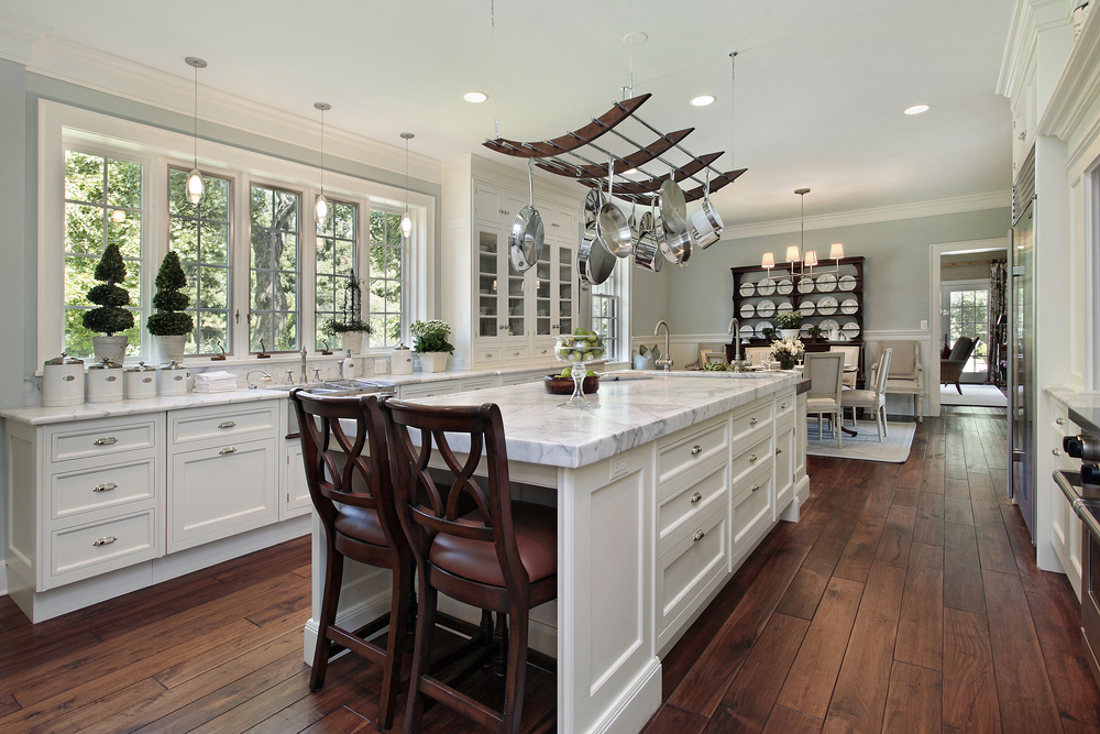 A bright kitchen with white marble countertops and wooden chairs.