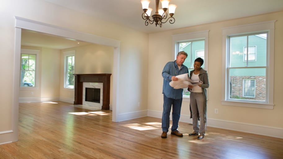 a homeowner and contractor look at renovation plans in an empty house