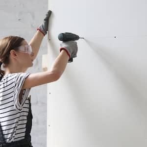 A woman wearing protective glasses assembling a closet by using an electric screwdriver