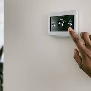 A hand adjusts the temperature of the room using a thermostat