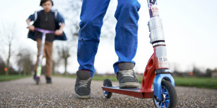 Children in park playing on micro scooters.