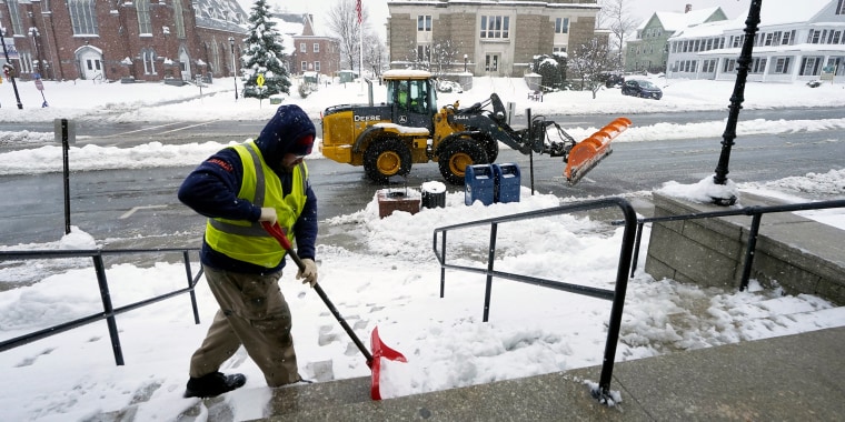 City worker Matt Houle, of Leominster, Mass., left, shovels the steps of Leominster City Hall, Tuesday, March 14, 2023, while a loader, behind, clears the street of snow, in Leominster. The New England states and parts of New York are bracing for a winter storm due to last into Wednesday. (AP Photo/Steven Senne)