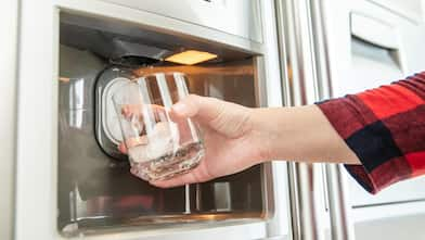 Woman's hand holds glass and uses refrigerator to make ice cubes