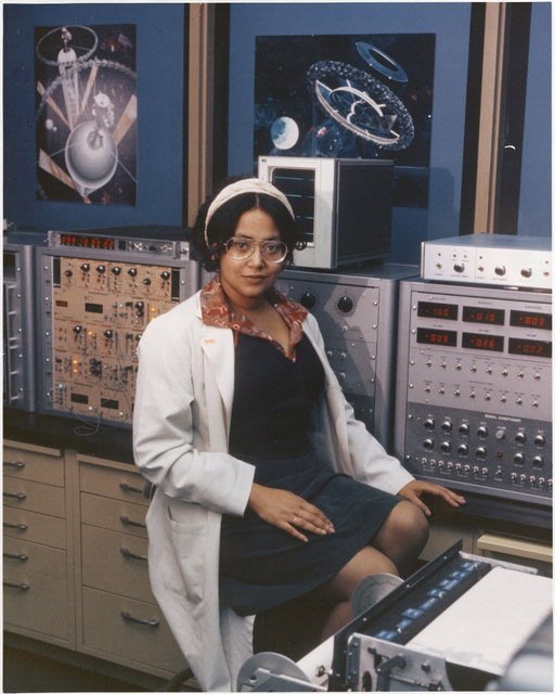 Patricia Cowings sitting on a stool in a white lab coat and looking directly at the camera. She is surrounded by scientific equipment.