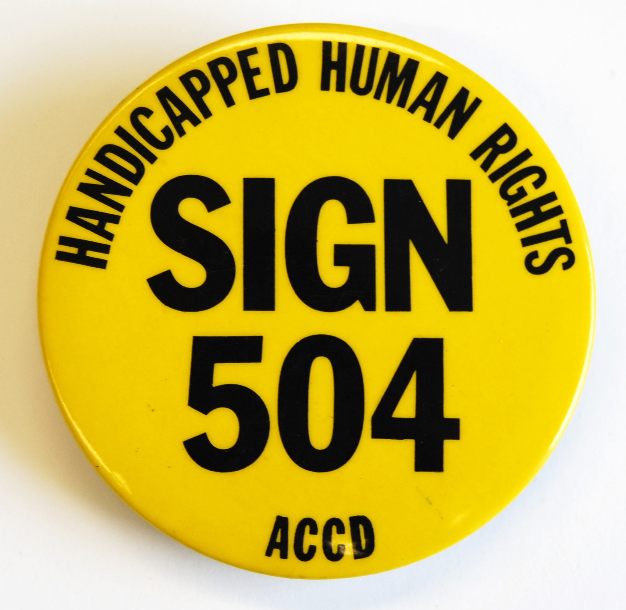 Yellow button with text: Handicapped human rights, sign 504, ACCD.