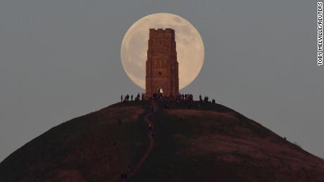 People stand beside St Michael&#39;s Tower as they watch the full moon, sometimes known as a &quot;Wolf Moon&quot;, rise behind Glastonbury Tor in Glastonbury, Britain, January 17, 2022. REUTERS/Toby Melville