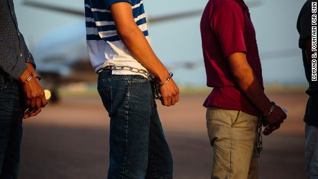 Deportees wait to be searched by guards before boarding the plane.