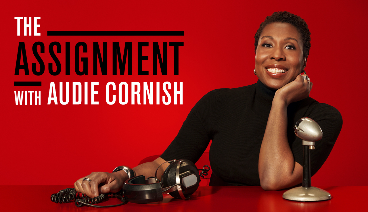 The Assignment with Audie Cornish cover art. Audie Cornish leaning back at a red desk with headphones and a microphone on it in a red space.