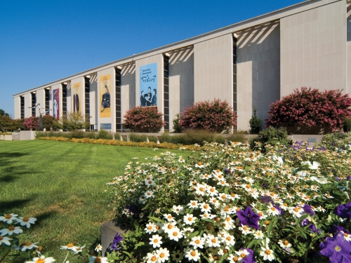 Exterior of Brutalist style building with green grass and flowers in front of it