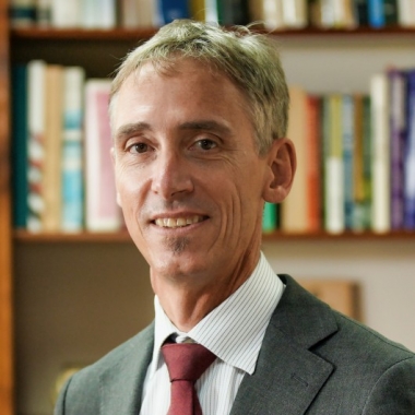 Man in a suit smiles with a bookcase behind him