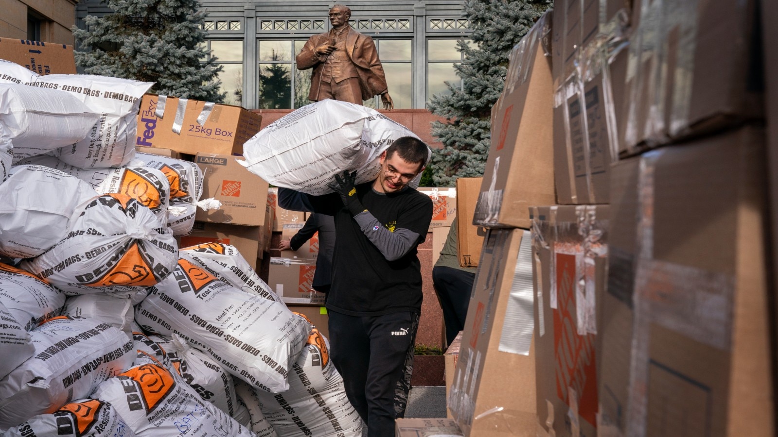 Man carrying large bag past high stacks of bags and boxes (© Jacquelyn Martin/AP)