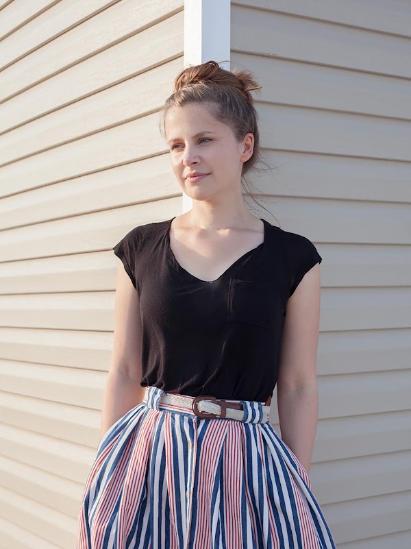 Thoka Maer, an Art Director on the Google Doodles team, stands against a wall. She wears a black shirt and her hair is up in a bun.