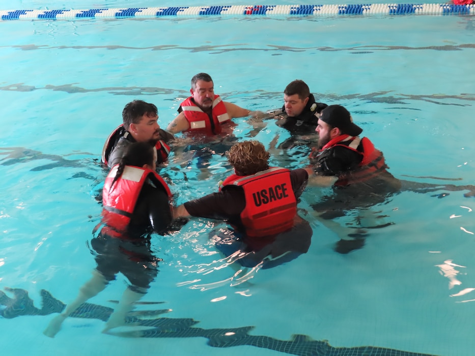 Team members gather in a circle in a pool and tread water as part of water safety training