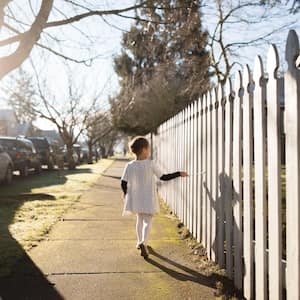Girl walking next to white picket fence