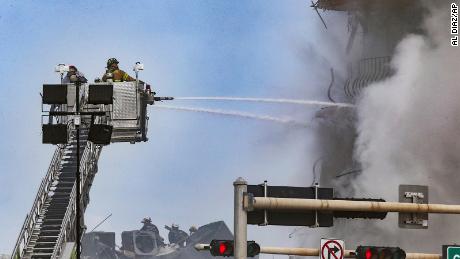 Firefighters battle a blaze as rescue workers search debris at the 12-story oceanfront condo, Champlain Towers South,  Friday, June 25, 2021 in Surfside, Fla. The apartment building partially collapsed on Thursday, June 24. (Al Diaz/Miami Herald via AP)