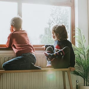 Kids sitting on a bench in front of a radiator watching out the window