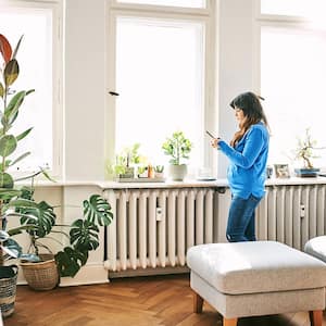 Woman stands by living room radiator looking at phone