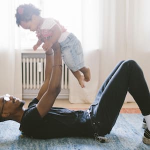 Father lifting daughter while lying on carpet at home