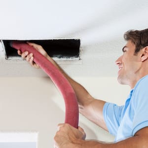 A man cleaning an air duct by using a vacuum cleaner