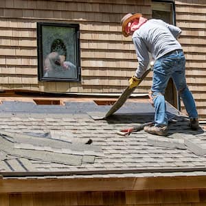 A man removes asphalt shingles from a roof