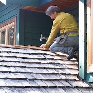 Roofer patches cedar shingles at roof ridgeline