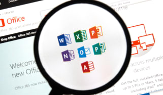 A magnifying glass hovering over a PC screen with the symbols for Microsoft Office software displayed