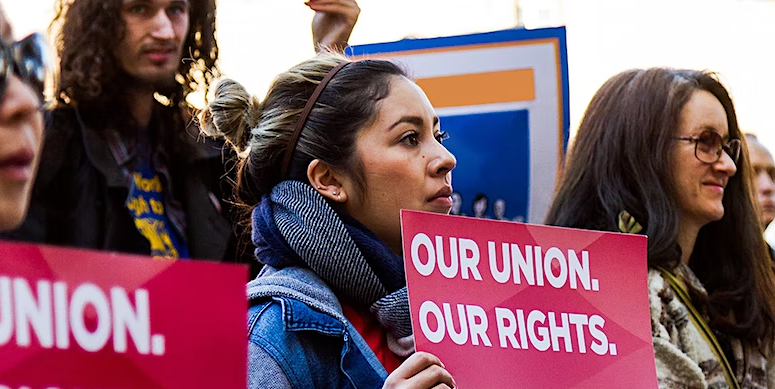 A woman participating in a protest holds a sign with the words Our union, our rights.