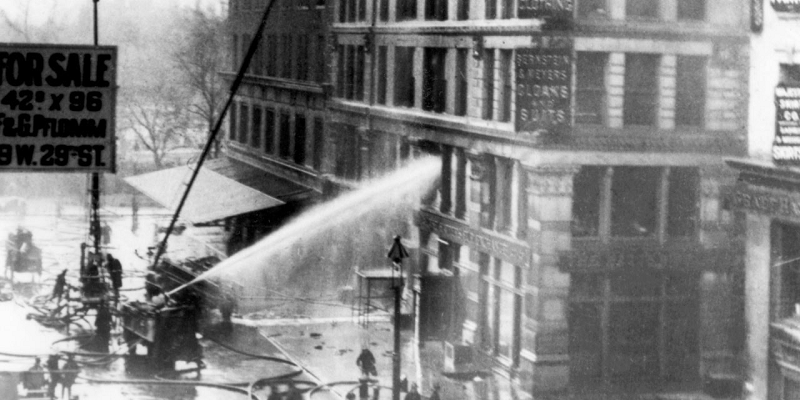 Black and white photo of firefighters spraying water to put out the fire at the Asch Building