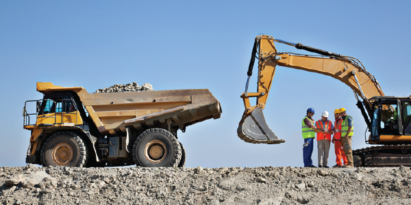 A group of construction workers stand by some large machinery on a worksite.