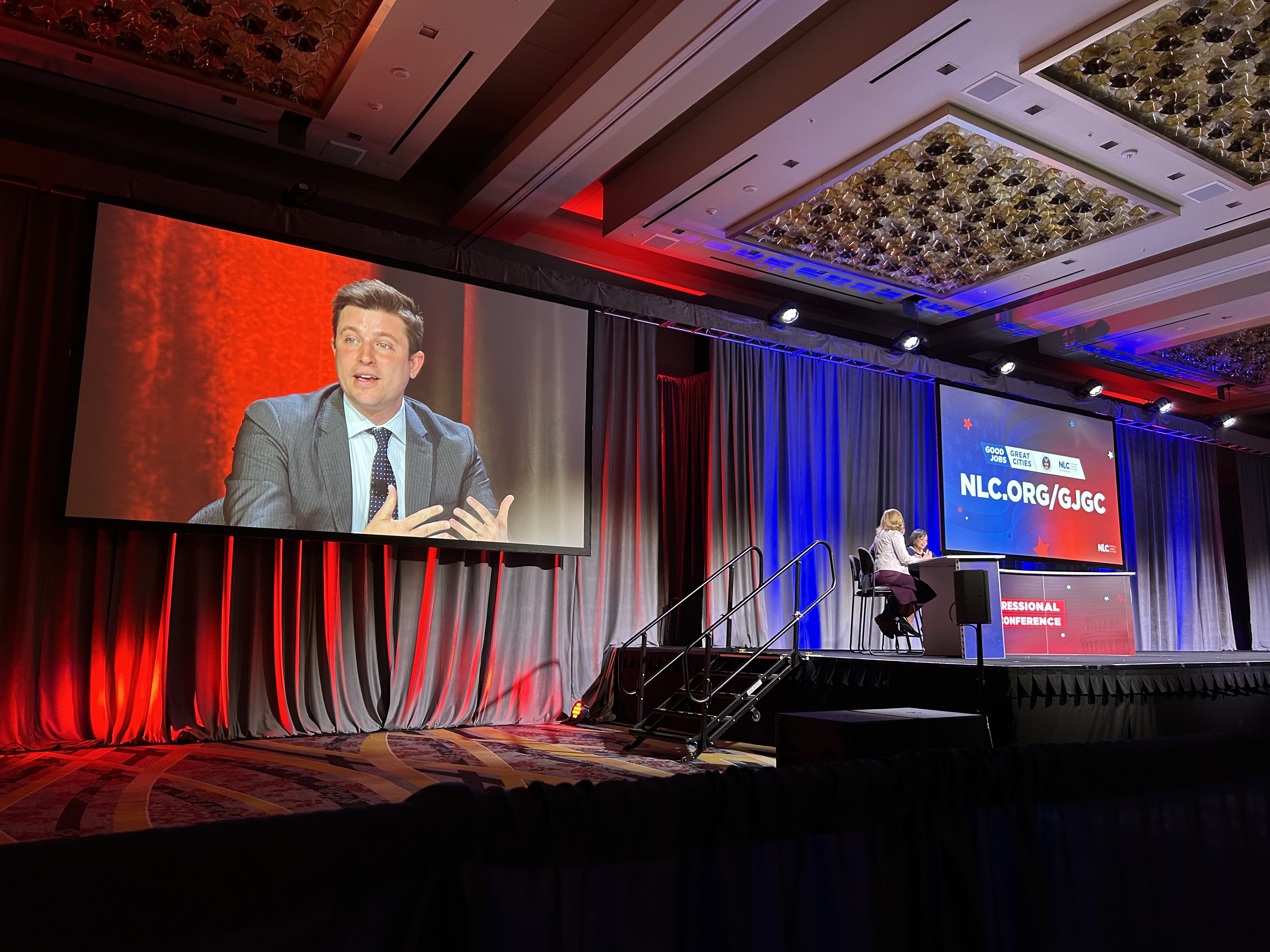 Brent Parton speaks on a stage. His face is projected on a monitor above the stage.