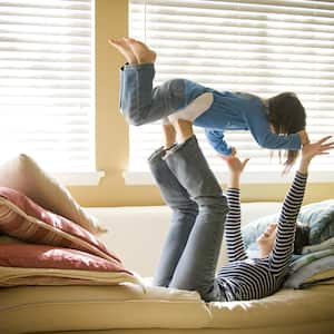 Mother playing with daughters in front of window with blinds