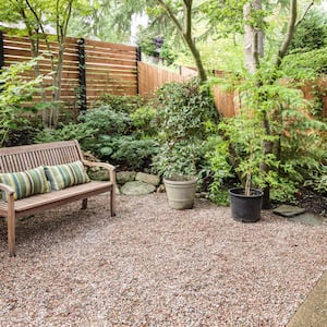 a light wood privacy fence surrounds a private yard with plants, bushes, a bench, and gravel