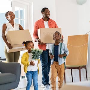 Family carrying cardboard boxes are entering their new home