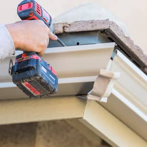 A man drills a gutter into the fascia board of a house 