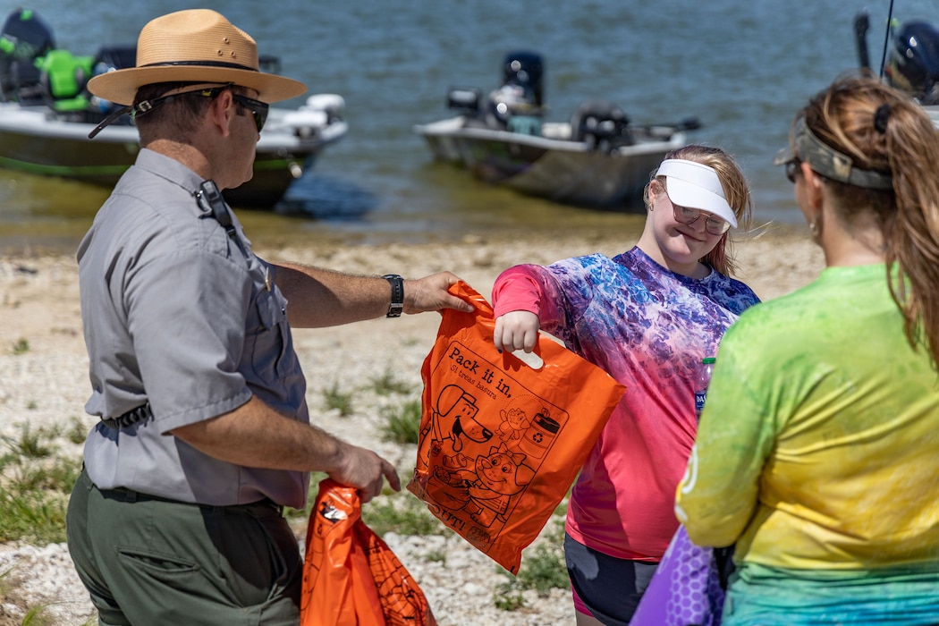 a park ranger in uniform talks to a child and her mother on the shoreline of a lake